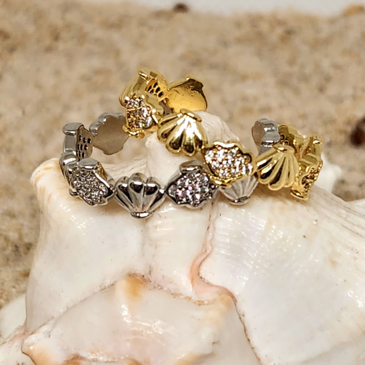 Gold and silver ring with heart and shell designs on a seashell.