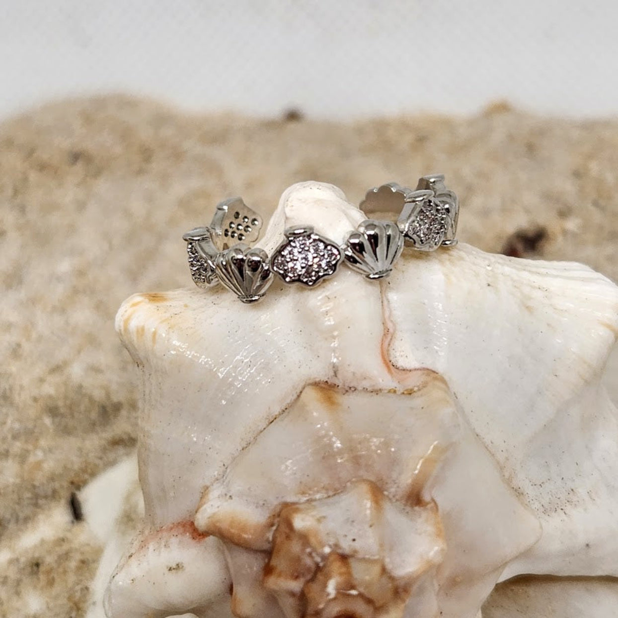 Silver ring with gemstones on a white shell against a beige background