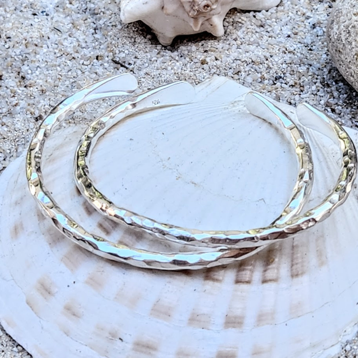 Silver bangle on a shell with sand and shells in the background