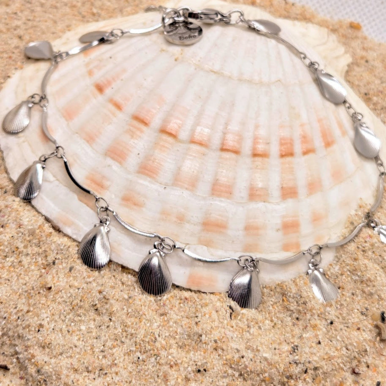 Silver bracelet with shell-shaped charms on a seashell against a sandy background