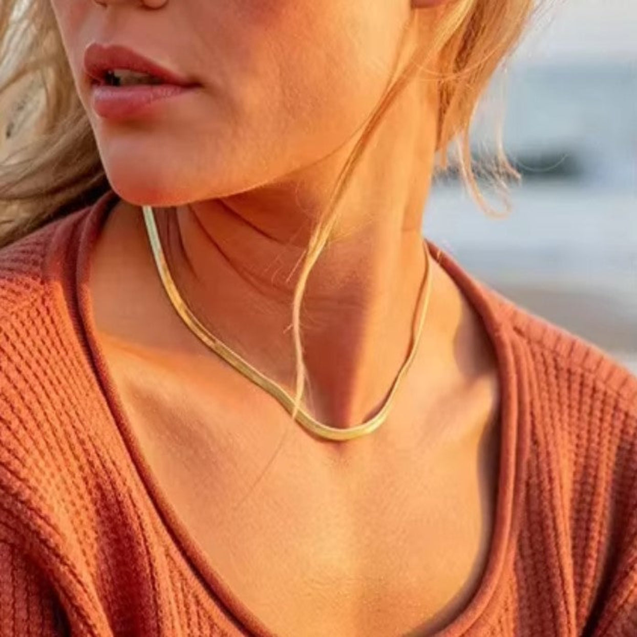 Close-up of a person wearing a gold necklace with a blurred background