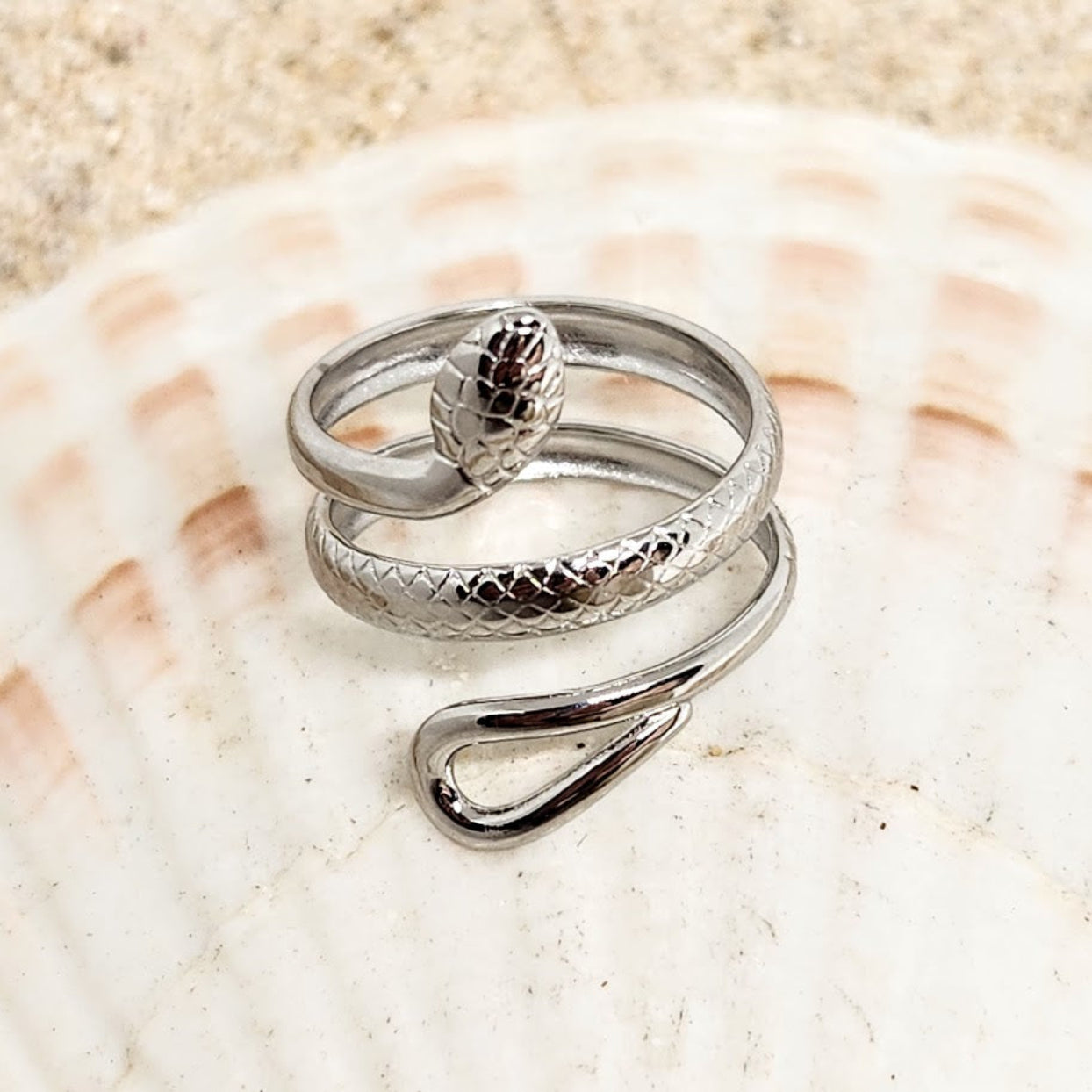 Silver ring with a textured design on a beige shell background