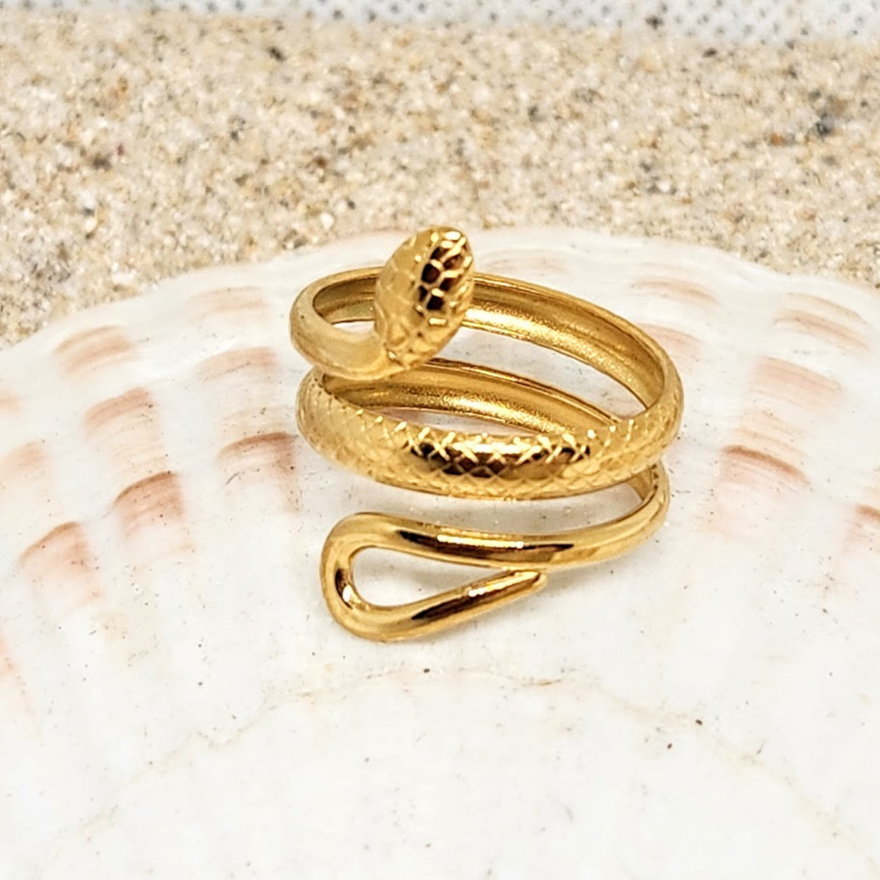 Gold snake-shaped ring on a seashell with sand background