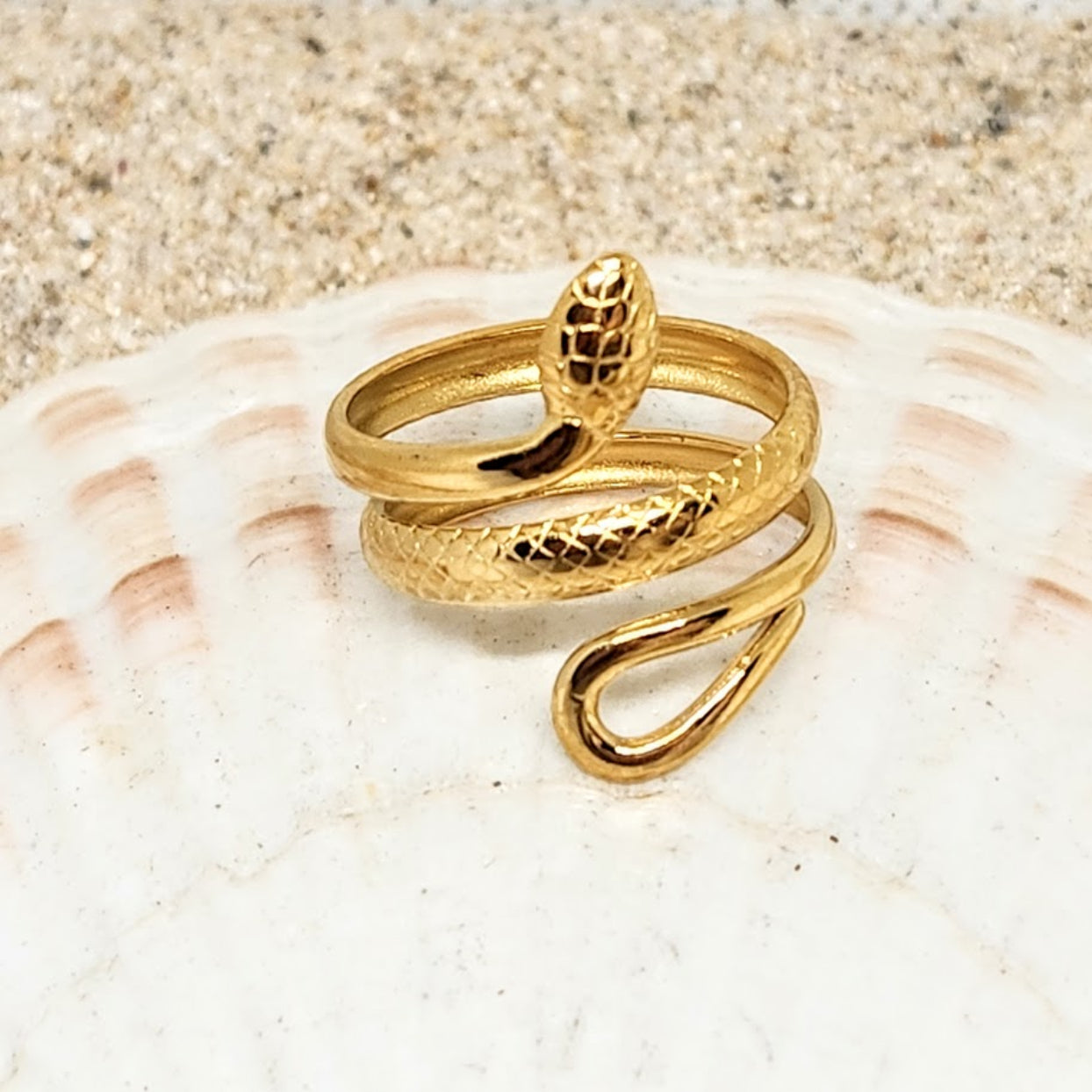 Gold snake-shaped ring on a seashell with a sandy background
