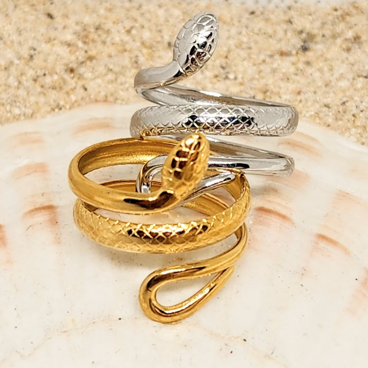 Two snake-shaped rings, one gold and one silver, on a seashell.
