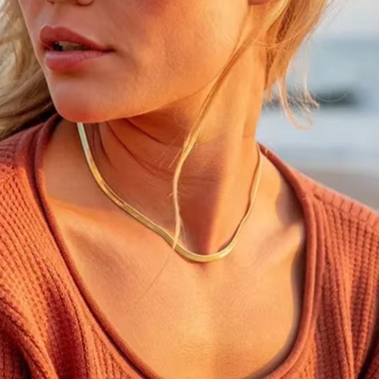 Close-up of a person wearing a gold necklace with a blurred background
