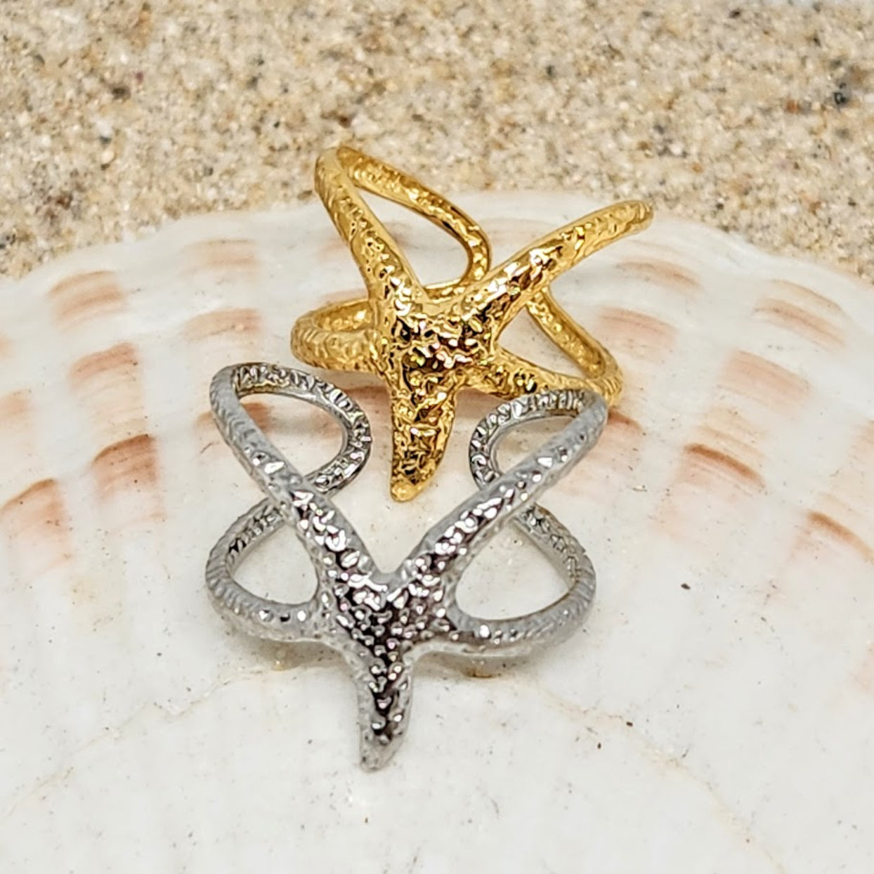 Gold and silver starfish-shaped rings on a seashell