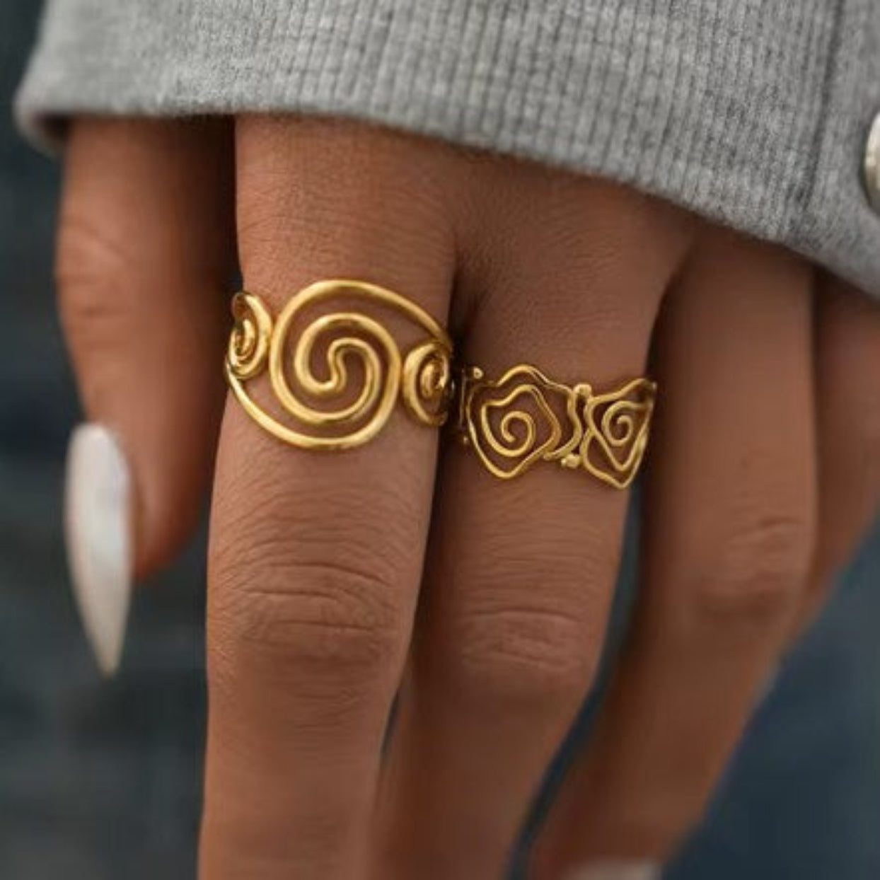 Gold ring with intricate design on a finger against a neutral background