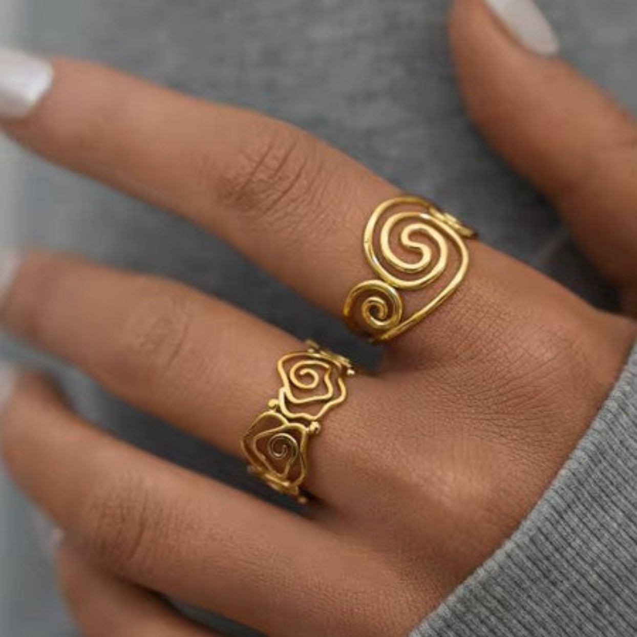 Gold spiral ring on a finger with a blurred gray background