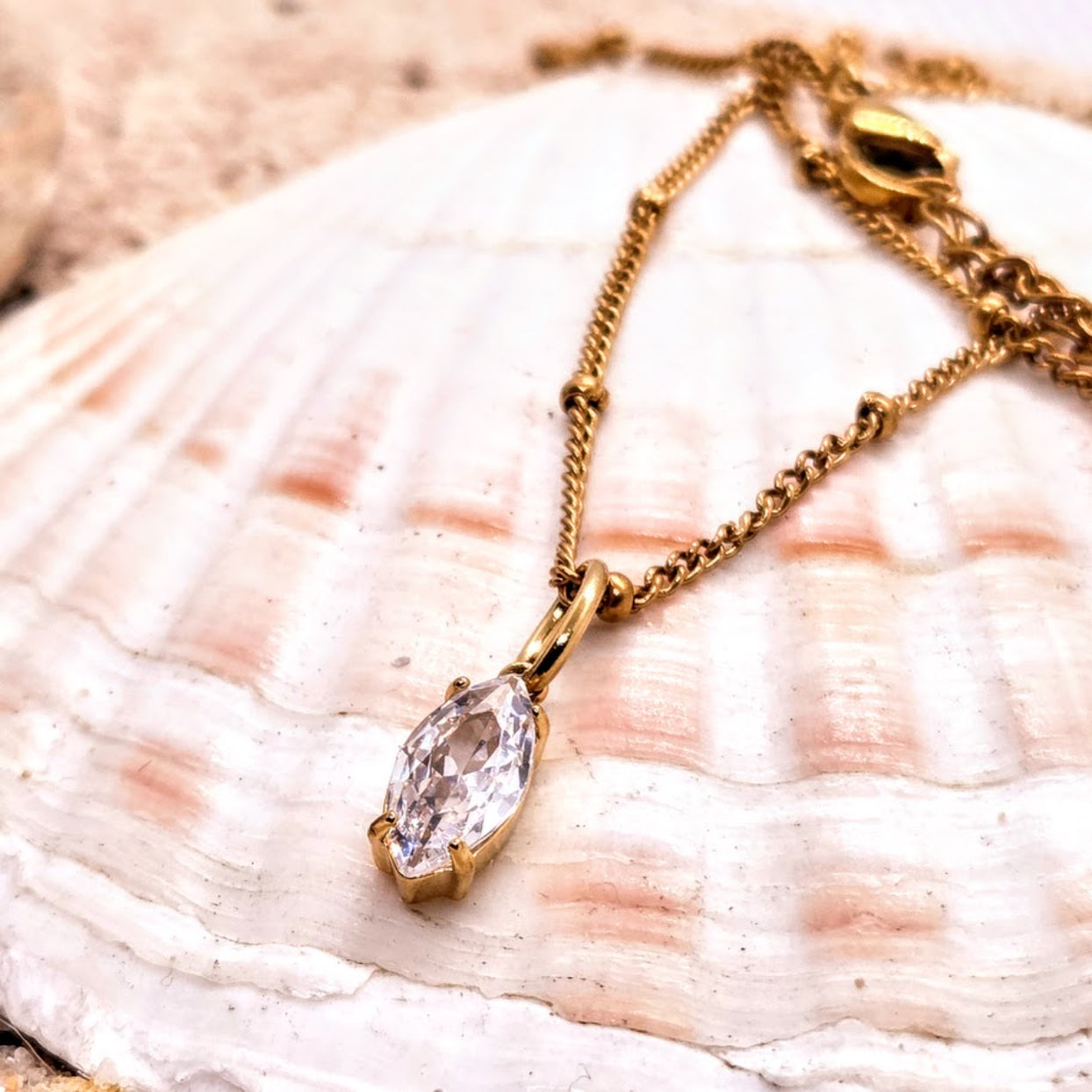 Gold necklace with a clear pendant on a seashell background