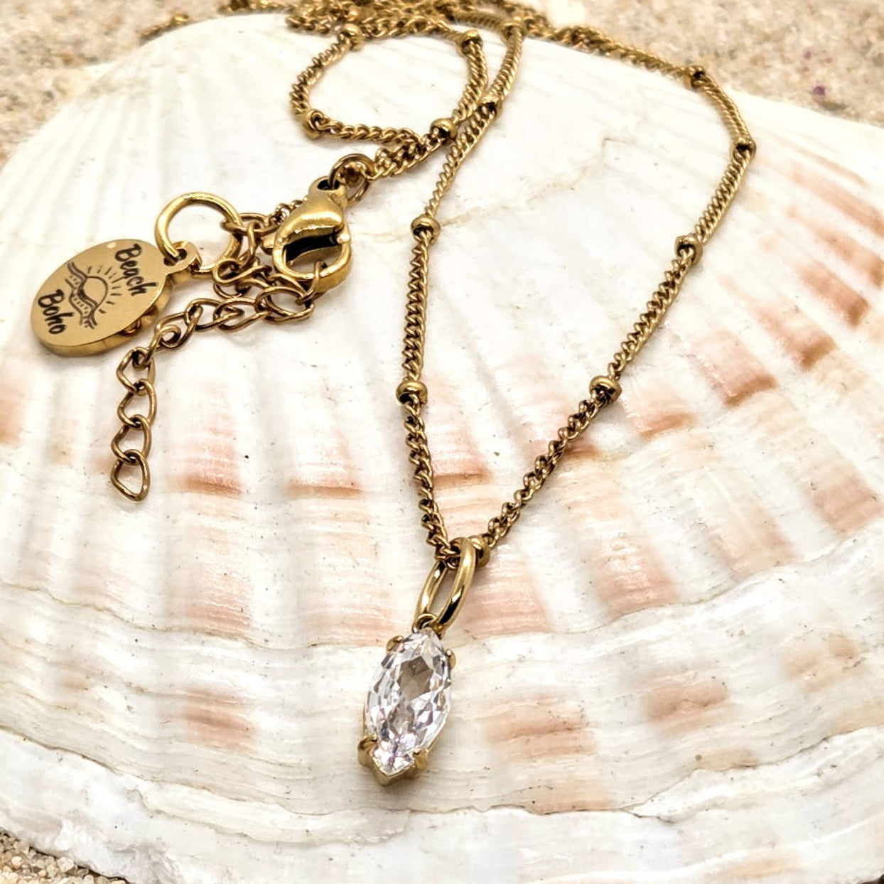 Gold necklace with a clear pendant on a seashell background