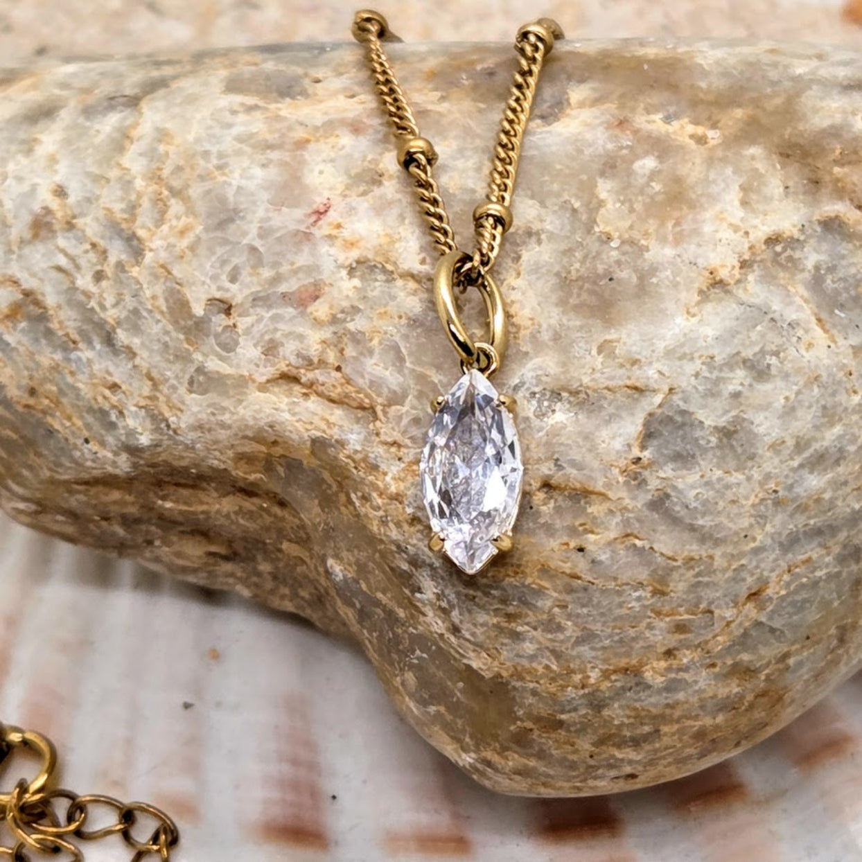 Gold necklace with a clear pendant on a textured stone surface
