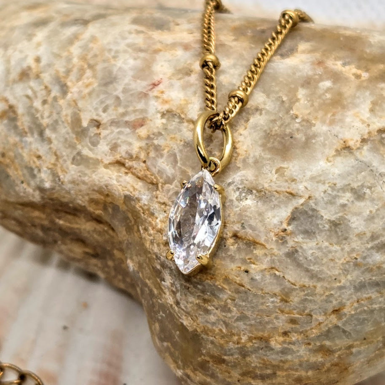 Gold necklace with a clear pendant on a textured stone surface