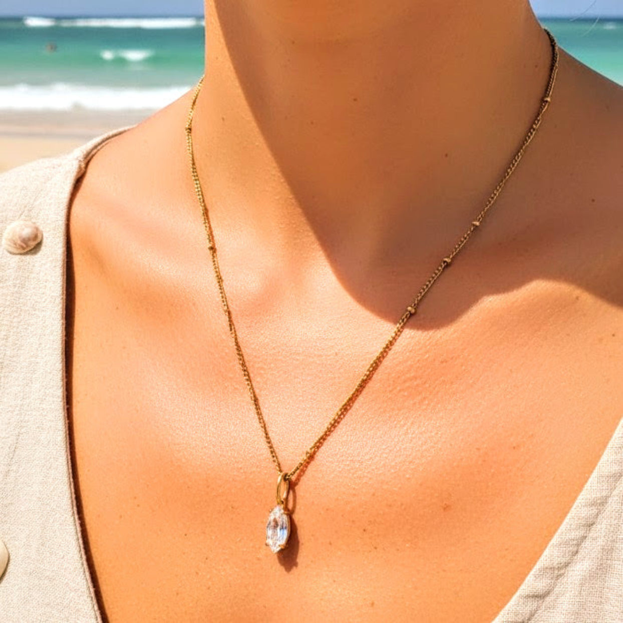 Gold necklace with a pendant worn by a person on a beach