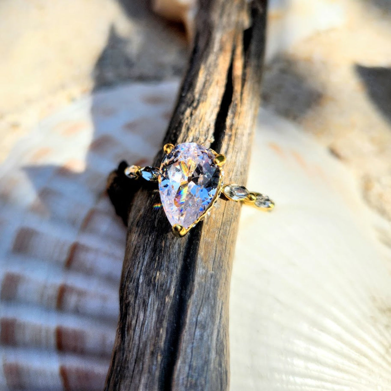 Gold ring with a colorful gemstone on a wooden stick and shell background