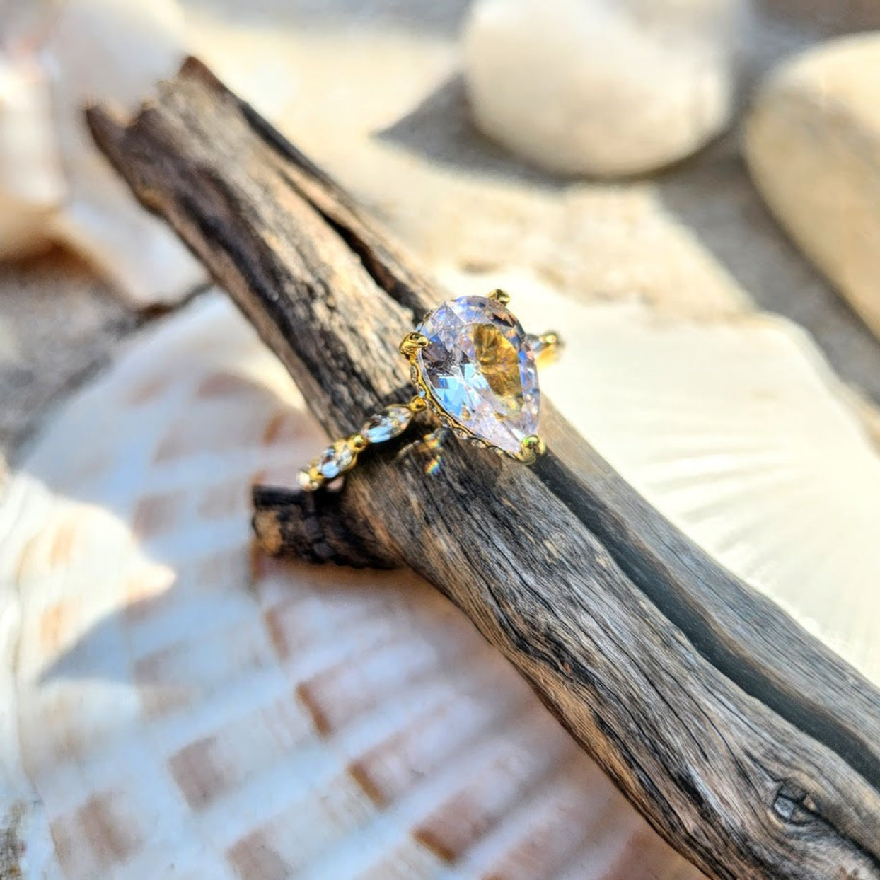 Gold ring with a clear gemstone on a piece of driftwood with seashells in the background