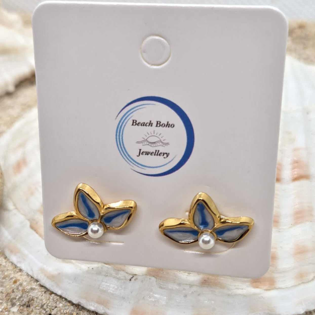 Butterfly-shaped earrings with pearls on a 'Beach Boho Jewellery' card, placed on a shell.