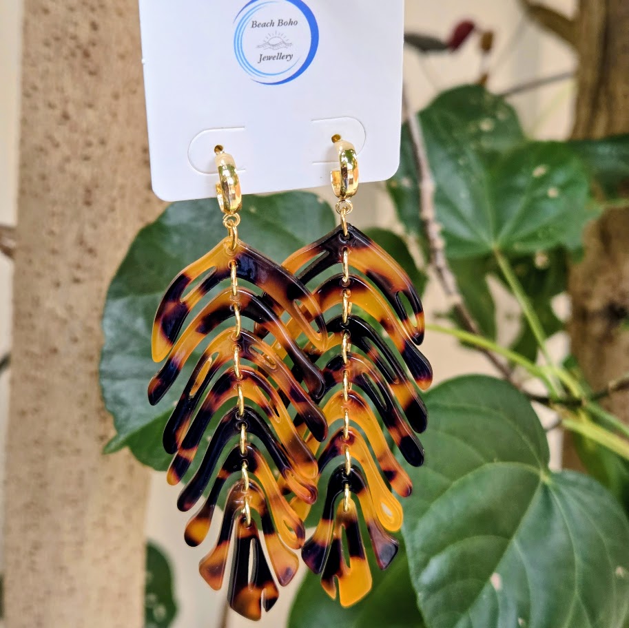 Tortoiseshell leaf-shaped earrings on a display card with green leaves in the background