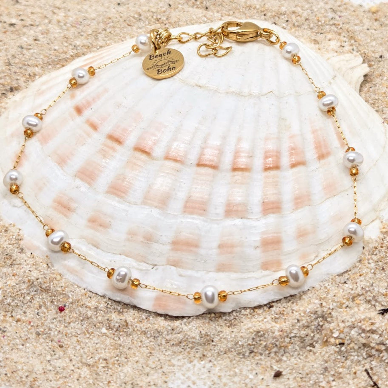 Pearl and gold bracelet on a seashell with sand background
