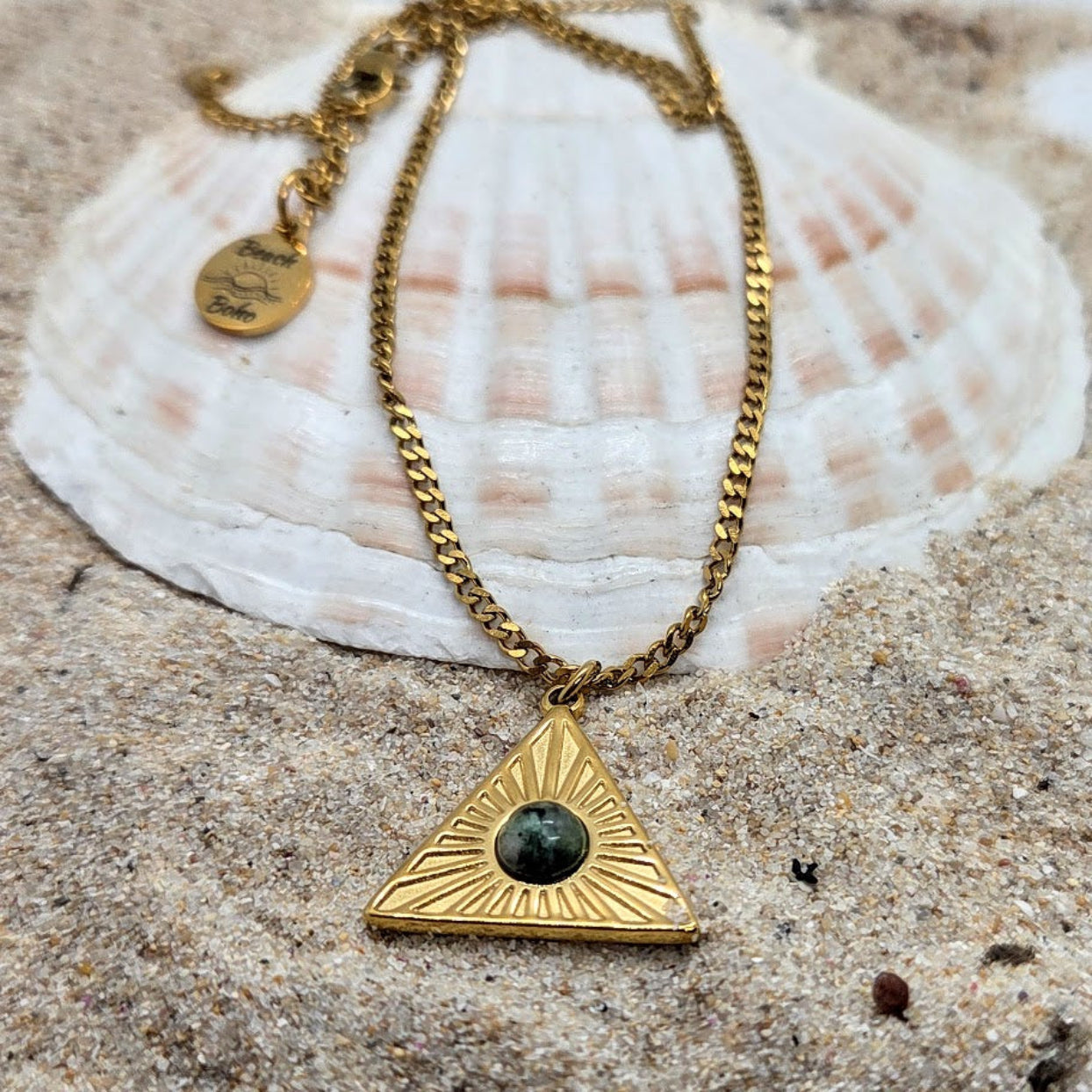 Gold necklace with a triangular pendant on a shell and sand background