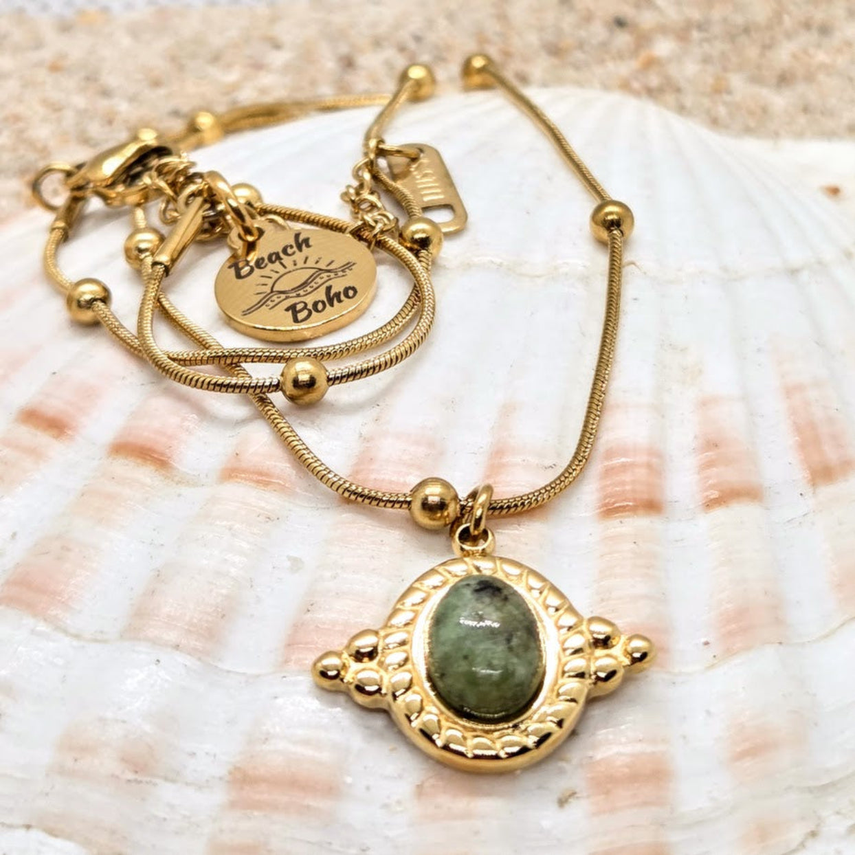 Gold bracelet with a green stone pendant on a seashell