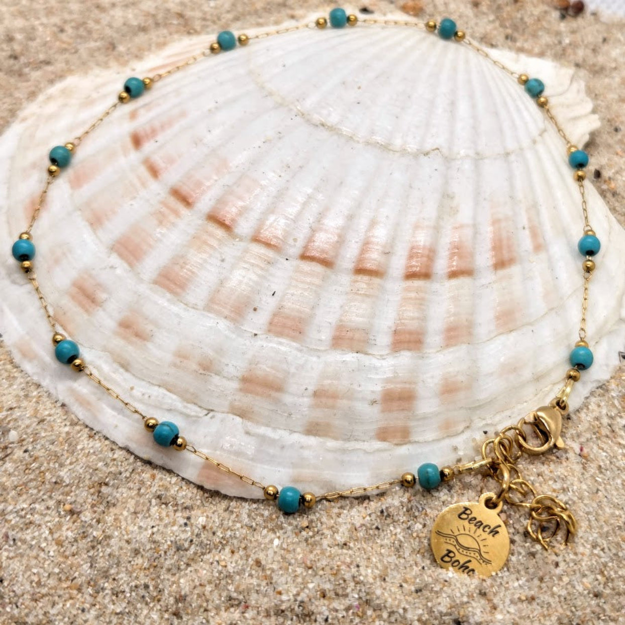 Necklace with blue beads and gold charm on a seashell in sand