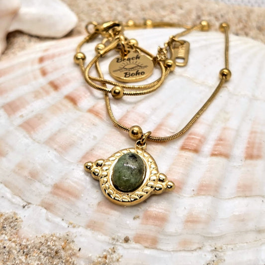 Gold bracelet with a green stone pendant on a seashell background