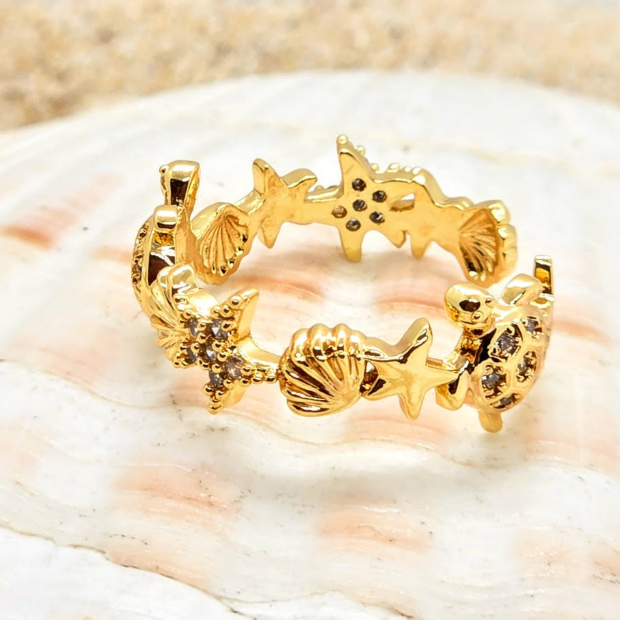 Gold ring with starfish and shell designs on a seashell background