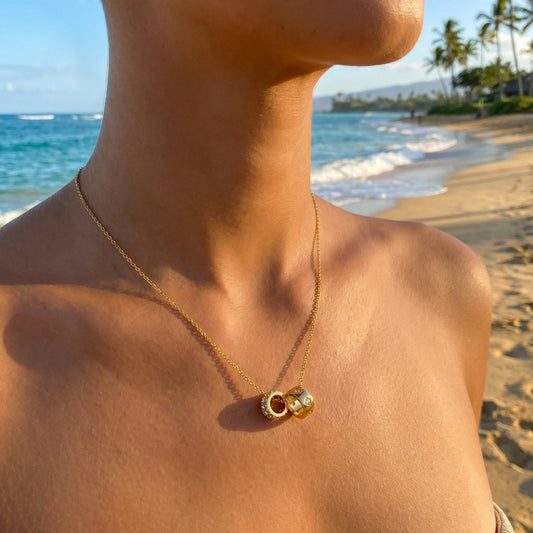 Person wearing a gold necklace with a pendant on a beach