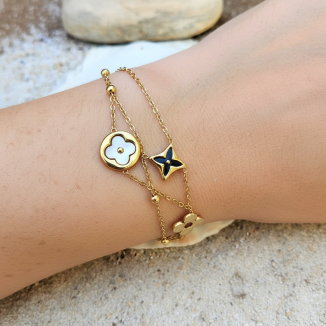 Gold bracelet with floral charms on a wrist against a natural background