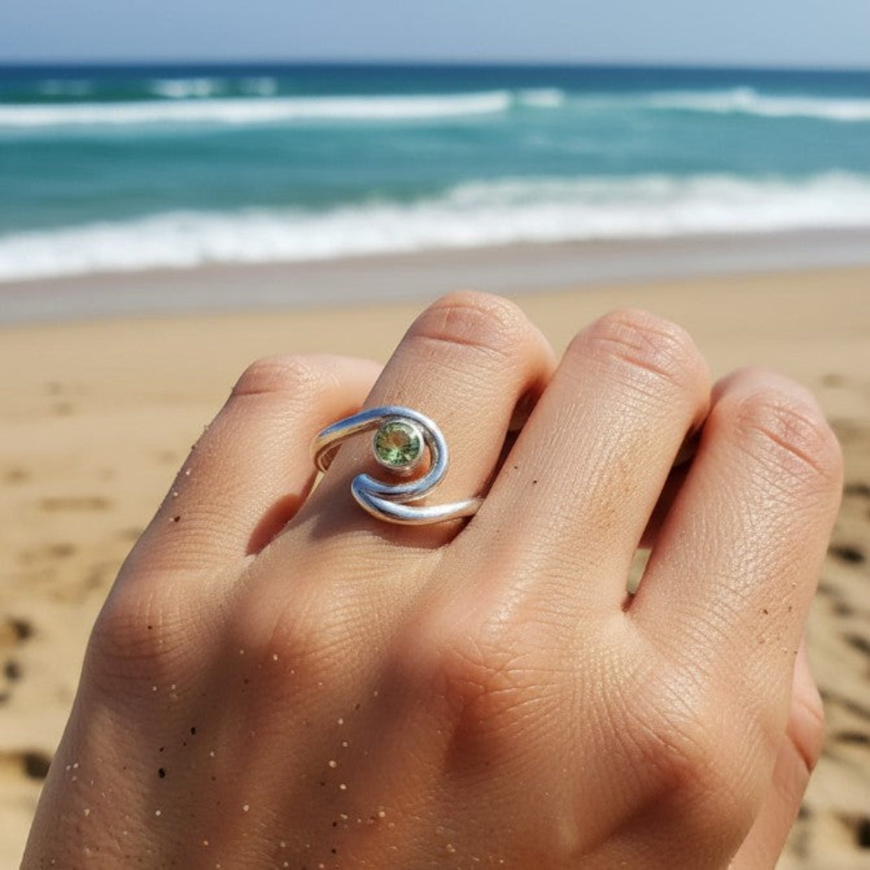 Hand wearing a silver ring with a green gemstone on a beach