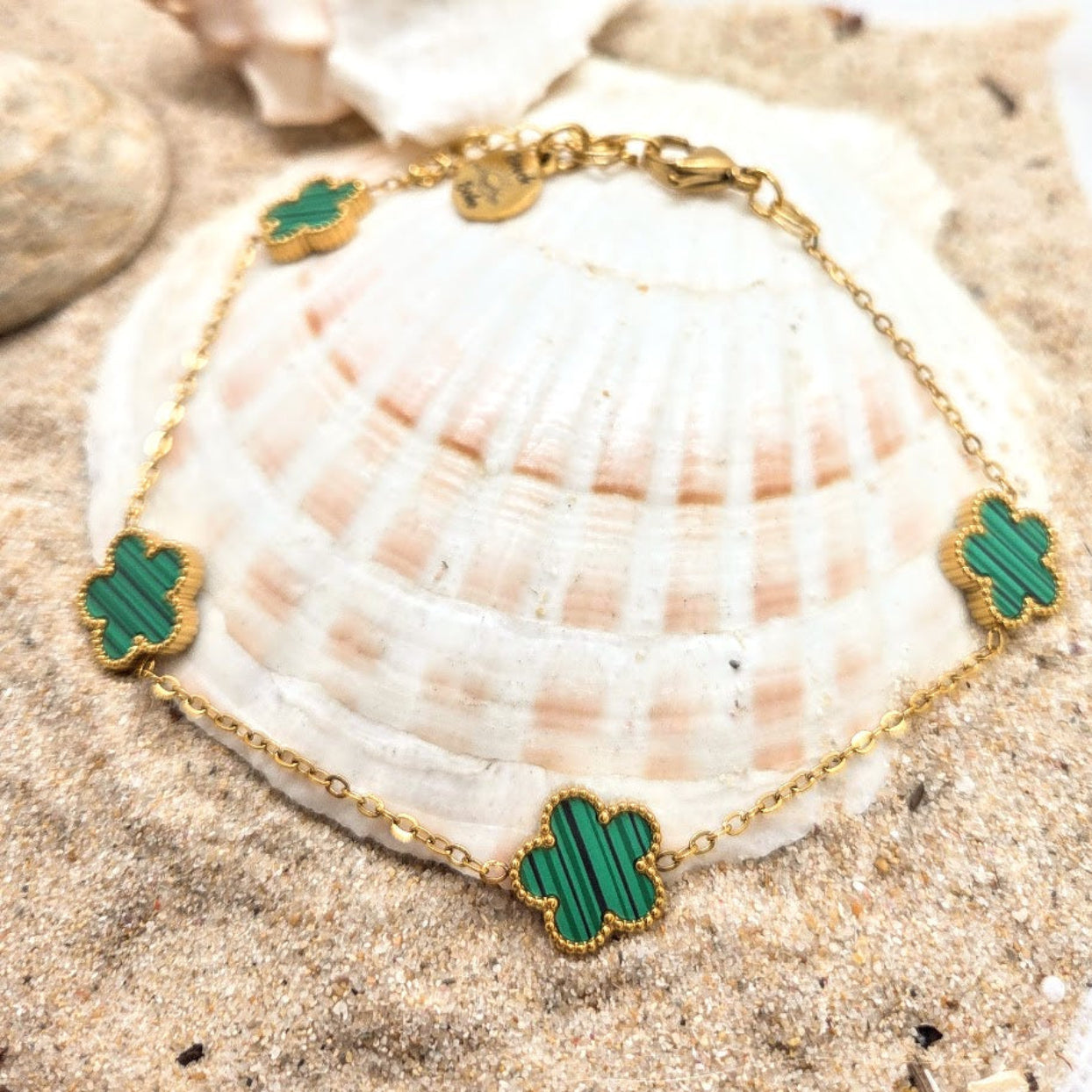 Gold bracelet with green accents on a seashell in sand