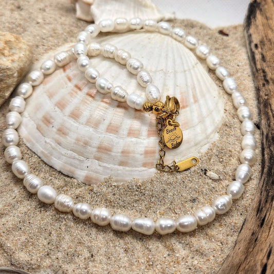 Pearl necklace with a gold charm on a seashell with sand and wood background