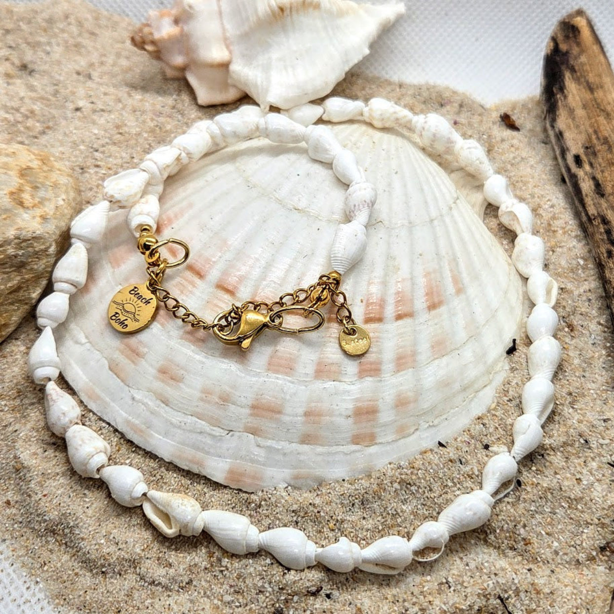 Shell bracelet with gold charms on a seashell with shells and sand in the background