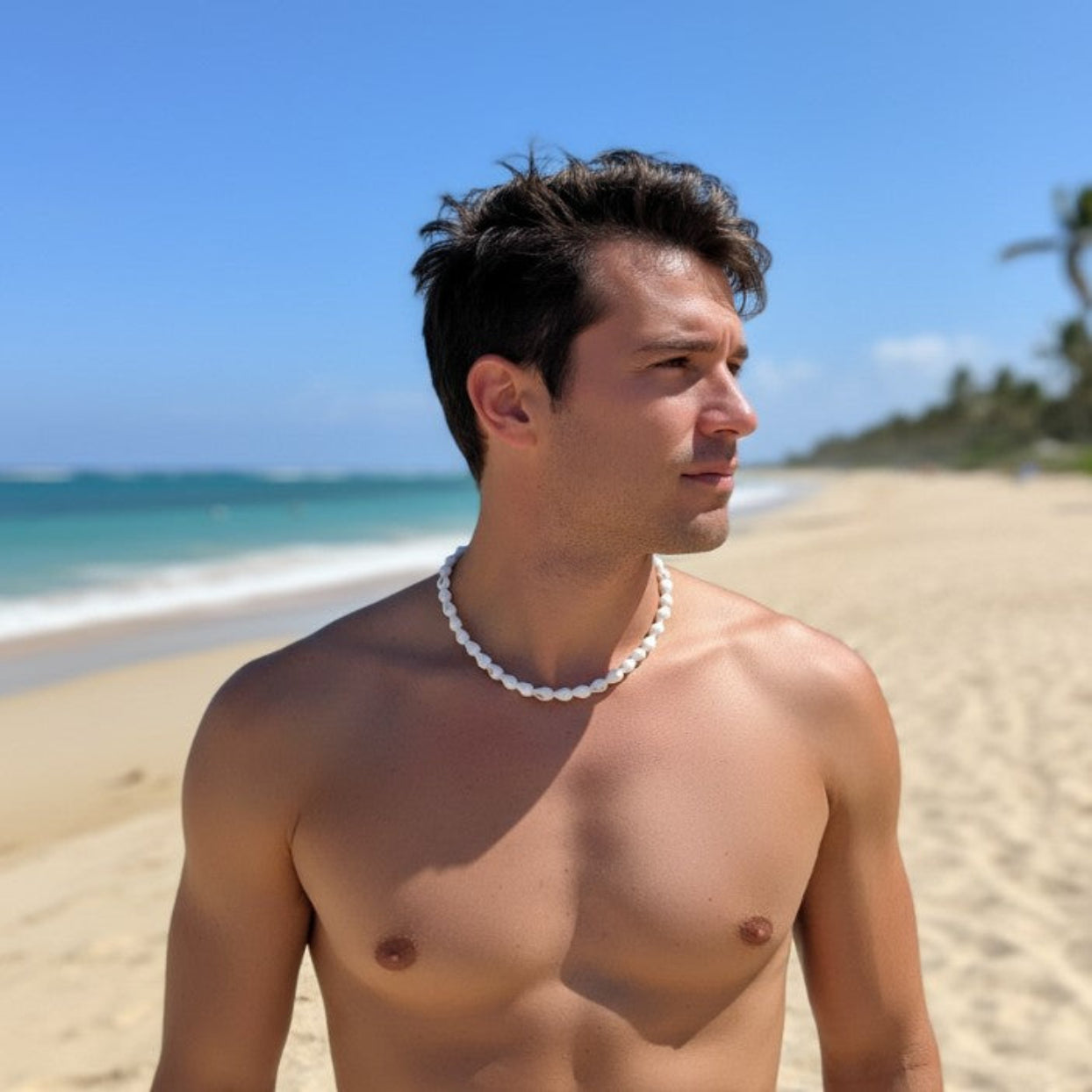 Man standing on a beach wearing a pearl necklace with clear blue sky and ocean in the background